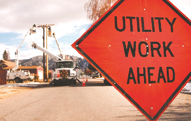 A caution sign in the foreground that reads "utility work ahead" with a line crew working in the background